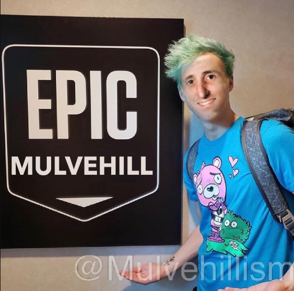 A candid photograph of Tim, green-haired, standing beside an EPIC MULVEHILL sign.